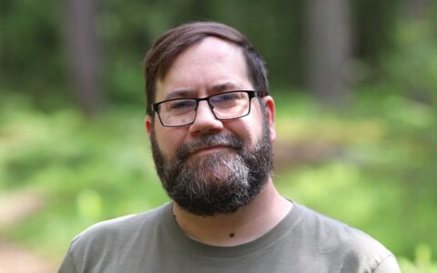 The man in the photo is smiling in a forest.