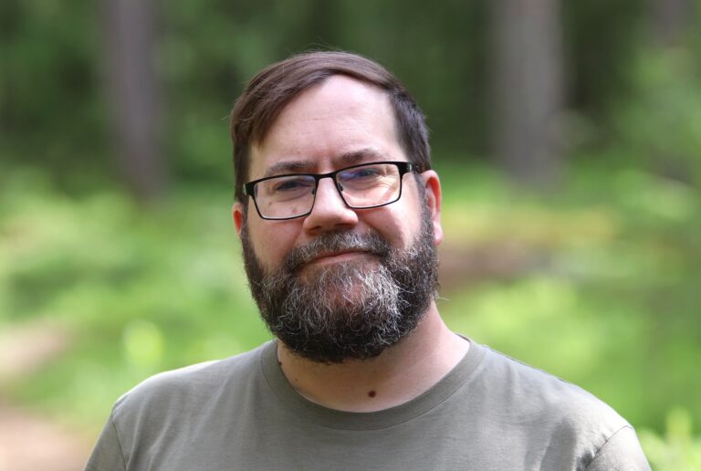 The man in the photo is smiling in a forest.