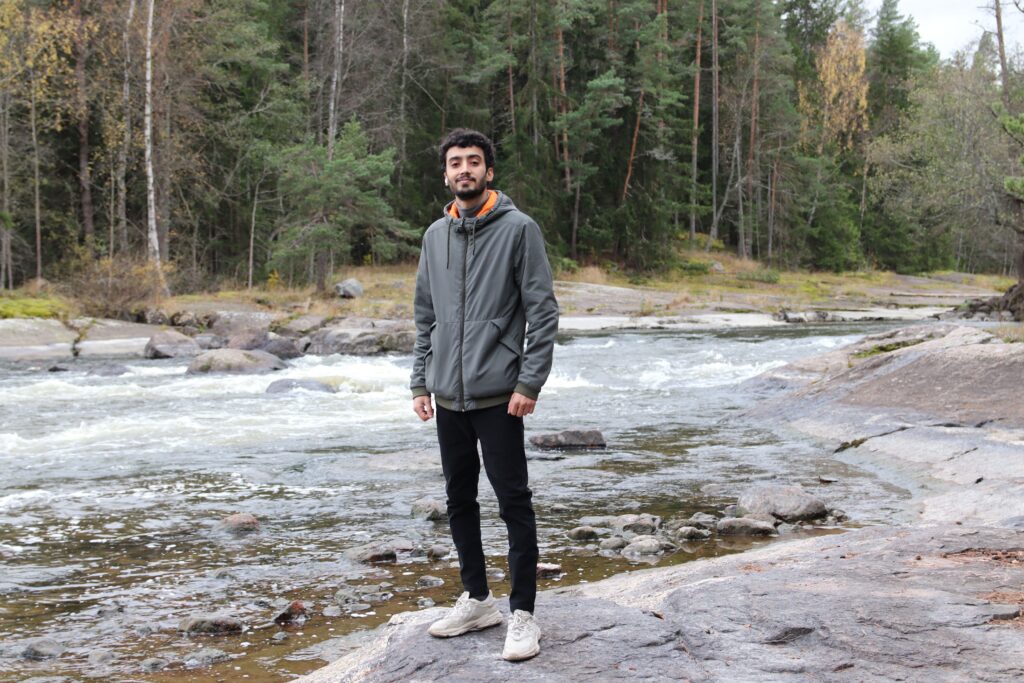 Mies seisoo kosken rannalla ja taustalla on metsää.